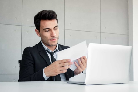 man holding envelope in front of a laptop